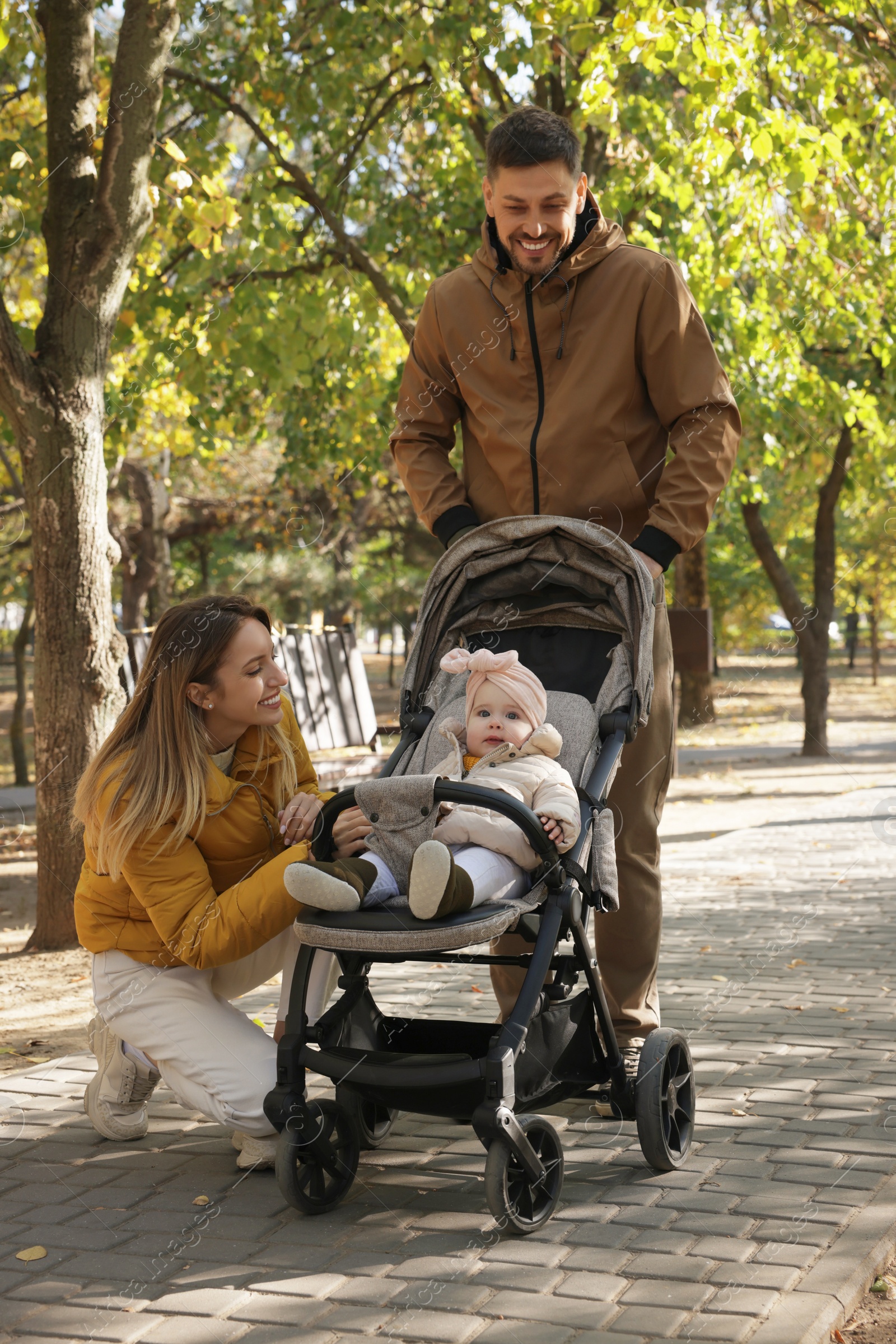 Photo of Happy parents walking with their baby in stroller at park on sunny day