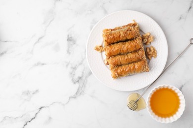 Photo of Eastern sweets. Pieces of tasty baklava and honey on white marble table, top view. Space for text