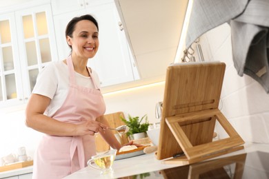 Photo of Woman making cake while watching online cooking course via tablet in kitchen
