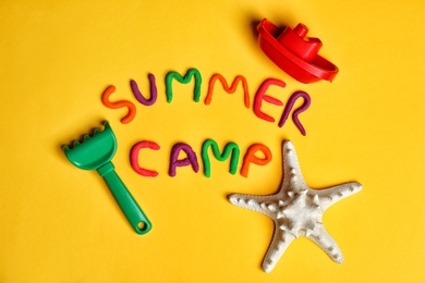 Photo of Flat lay composition with words SUMMER CAMP made from modelling clay and beach toys on color background