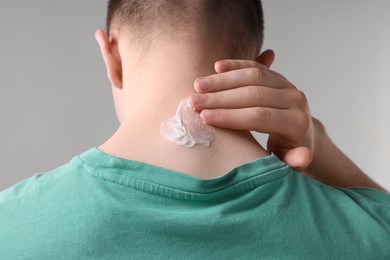 Man applying ointment onto his neck on light grey background, closeup
