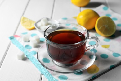 Photo of Cup of delicious ginger tea, sugar cubes and lemons on white wooden table, closeup