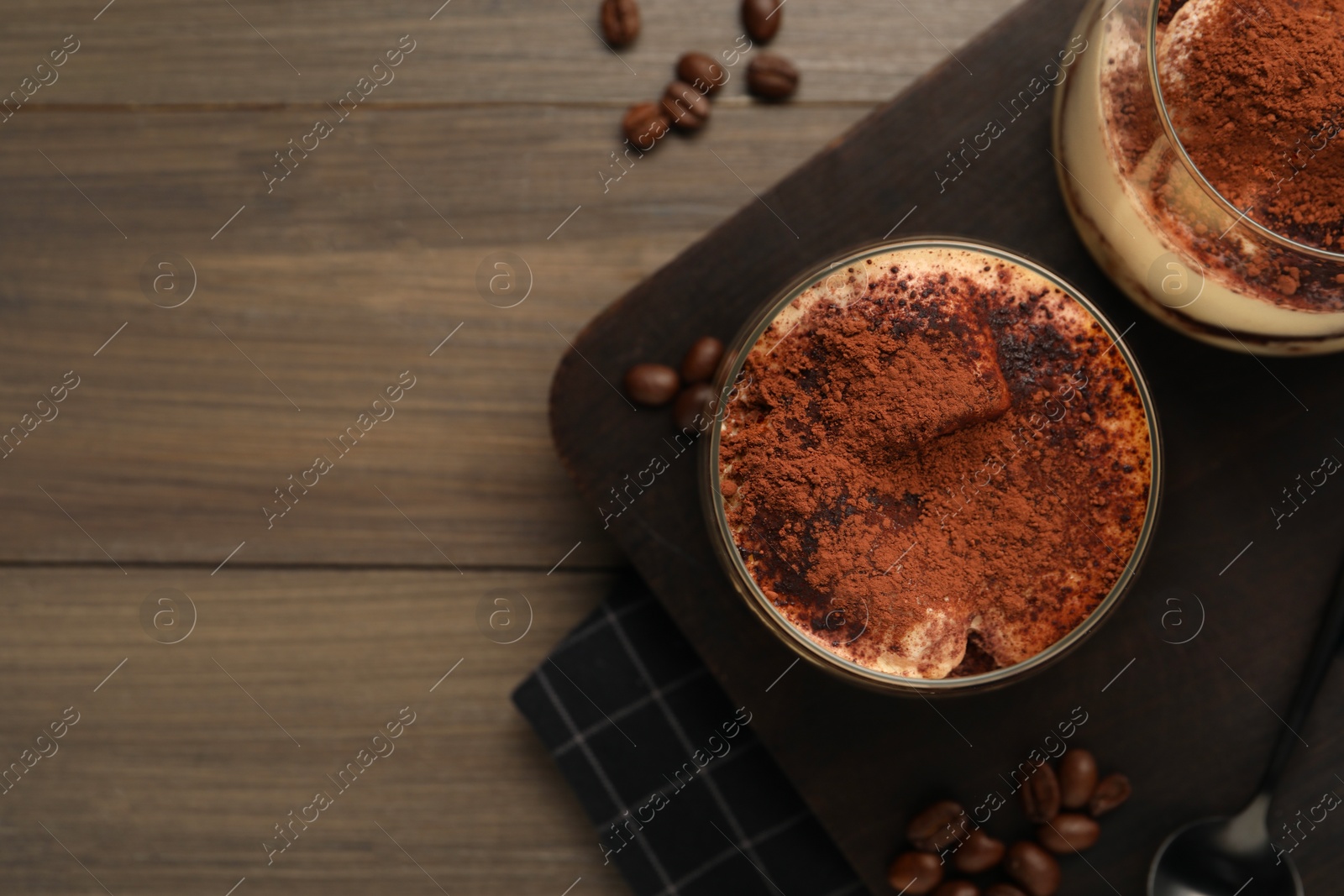 Photo of Delicious tiramisu in glasses and coffee beans on wooden table, top view. Space for text