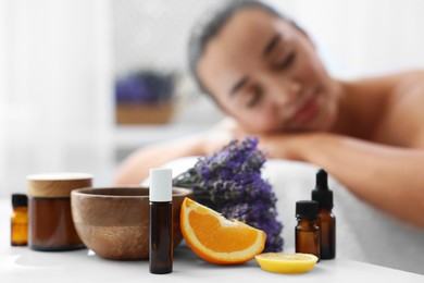 Photo of Woman relaxing on massage couch and bottles of essential oil with ingredients on table in spa salon, selective focus