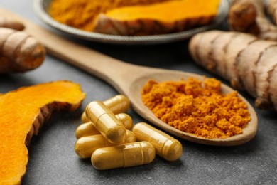 Photo of Aromatic turmeric powder, pills and raw roots on grey table, closeup