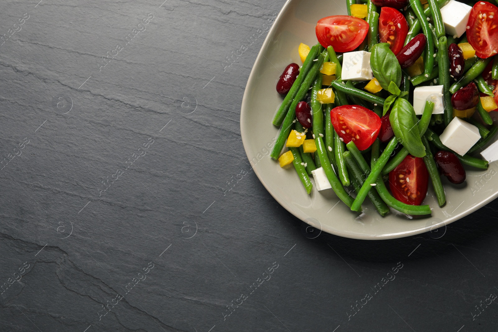Photo of Plate of tasty salad with green beans on black table, top view. Space for text