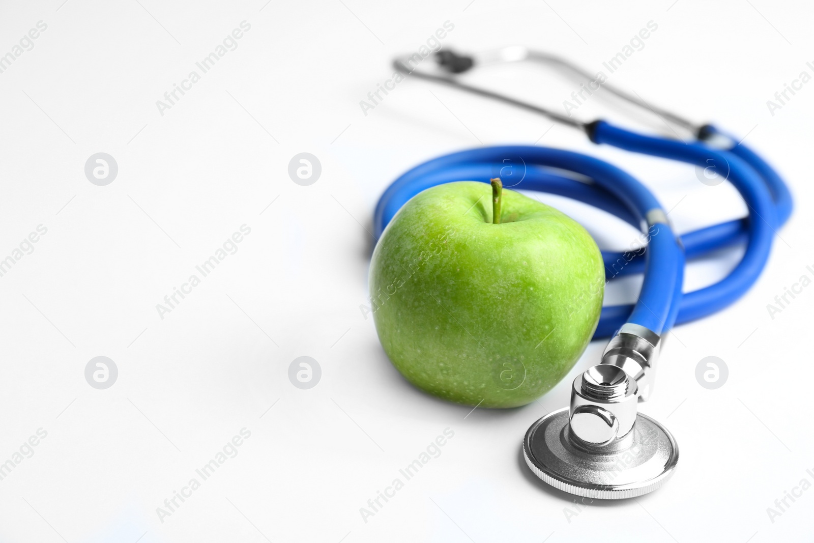 Photo of Stethoscope and apple on light background. Medical equipment