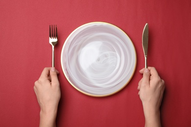 Woman with fork, knife and empty plate on color background, top view