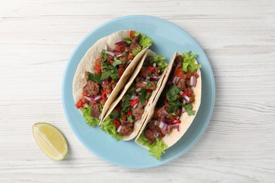 Delicious tacos with meat, vegetables and lime on wooden table, flat lay