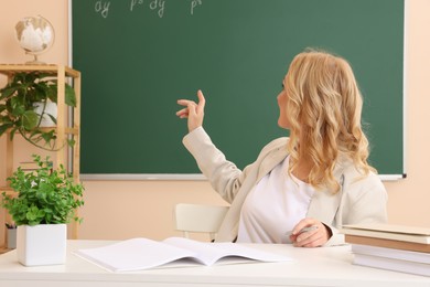 Professor pointing at green board with math equation in classroom