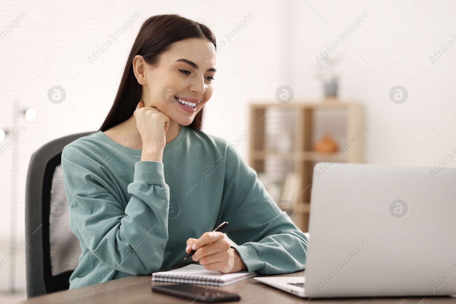 Photo of Young woman watching webinar at table in room