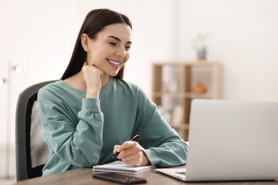 Young woman watching webinar at table in room