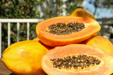 Fresh ripe cut and whole papaya fruits on wooden table outdoors, closeup