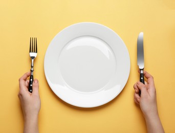 Photo of Woman with empty plate and cutlery on yellow background, top view