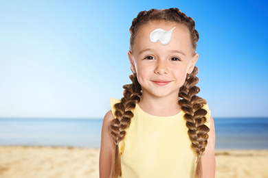 Adorable little girl with sun protection cream on face at sandy beach