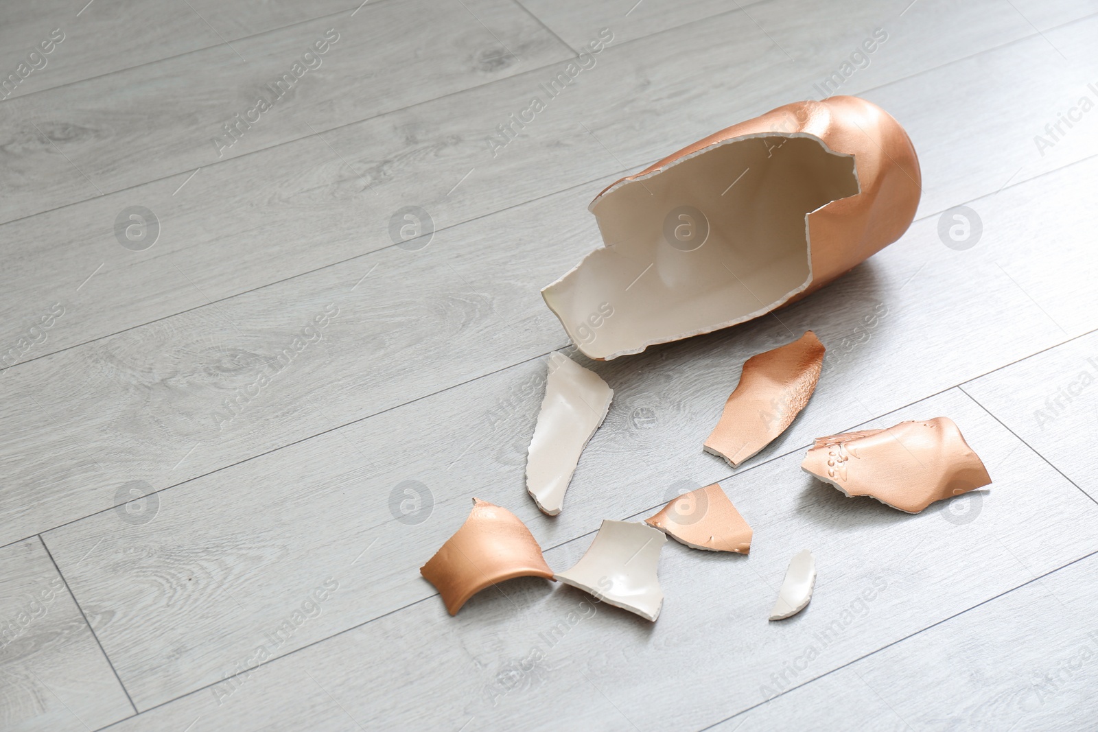 Photo of Broken golden ceramic vase on wooden floor, closeup. Space for text