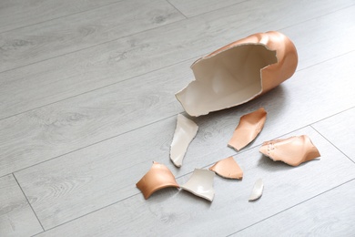 Broken golden ceramic vase on wooden floor, closeup. Space for text