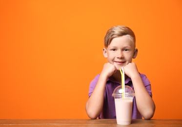 Photo of Little boy with cup of milk shake at table on color background