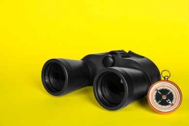 Photo of Modern binoculars and compass on yellow background
