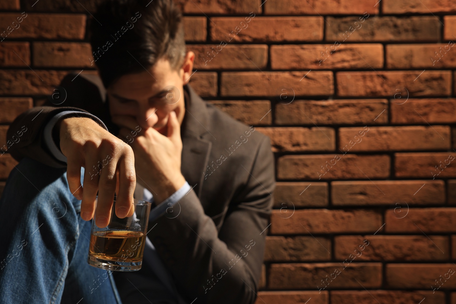 Photo of Addicted man near red brick wall, focus on glass of alcoholic drink. Space for text