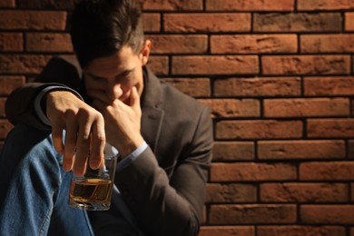 Photo of Addicted man near red brick wall, focus on glass of alcoholic drink. Space for text