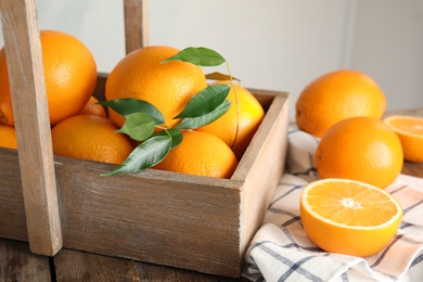 Fresh oranges with leaves and rustic box on wooden table