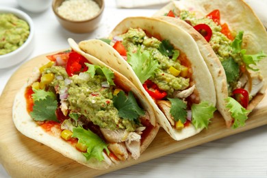 Delicious tacos with guacamole, meat and vegetables served on white wooden table, closeup