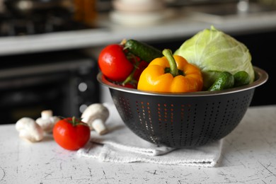 Metal colander with different wet vegetables on white textured table