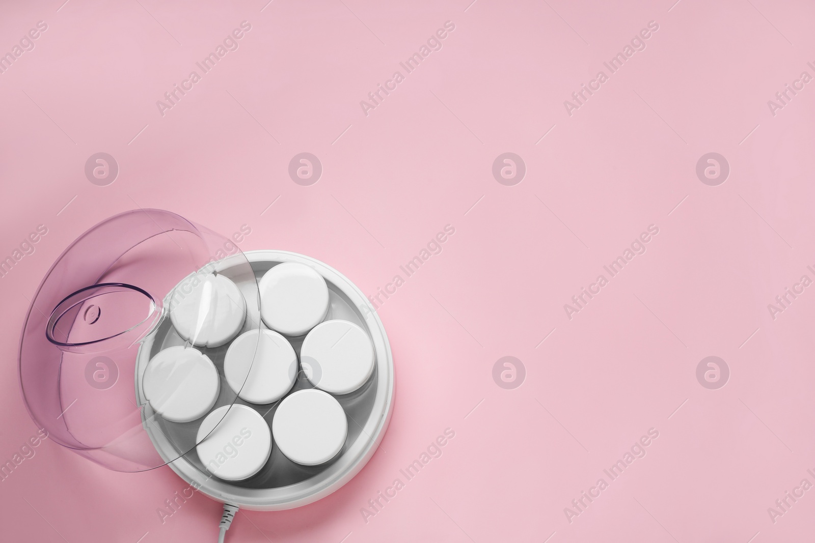 Photo of Modern yogurt maker with jars on pink background, top view. Space for text