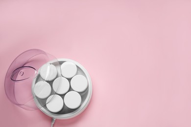 Photo of Modern yogurt maker with jars on pink background, top view. Space for text