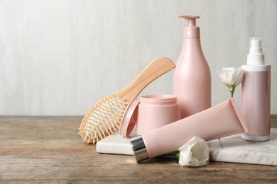 Photo of Different hair products, flower and brush on wooden table. Space for text