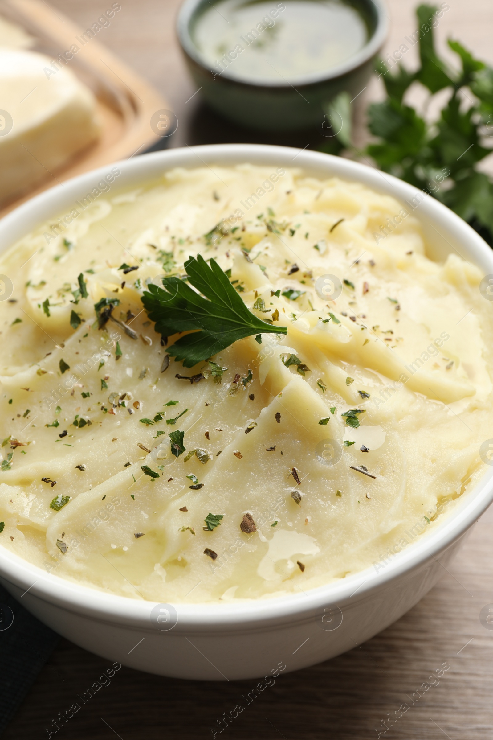 Photo of Bowl of delicious mashed potato with parsley on wooden table, closeup