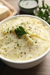 Photo of Bowl of delicious mashed potato with parsley on wooden table, closeup