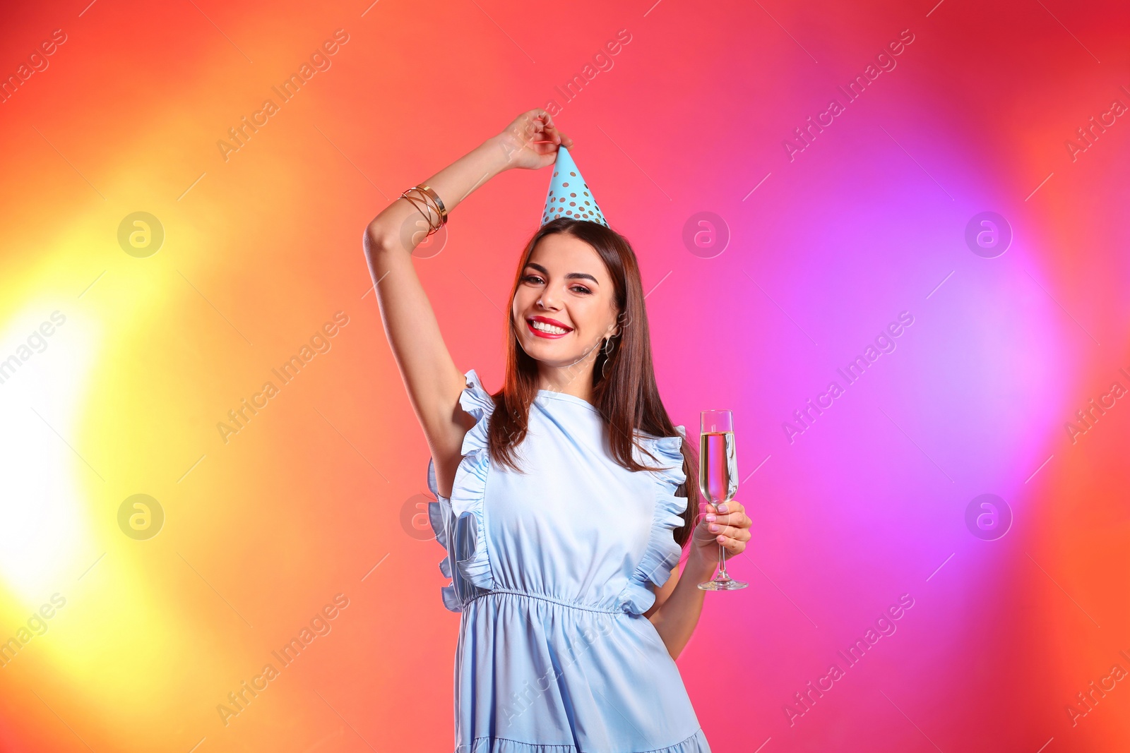 Photo of Portrait of happy woman with party hat and champagne in glass on color background