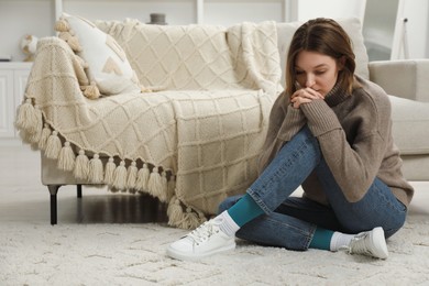 Photo of Sad young woman sitting on floor at home, space for text