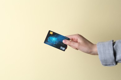 Woman holding credit card on beige background, closeup