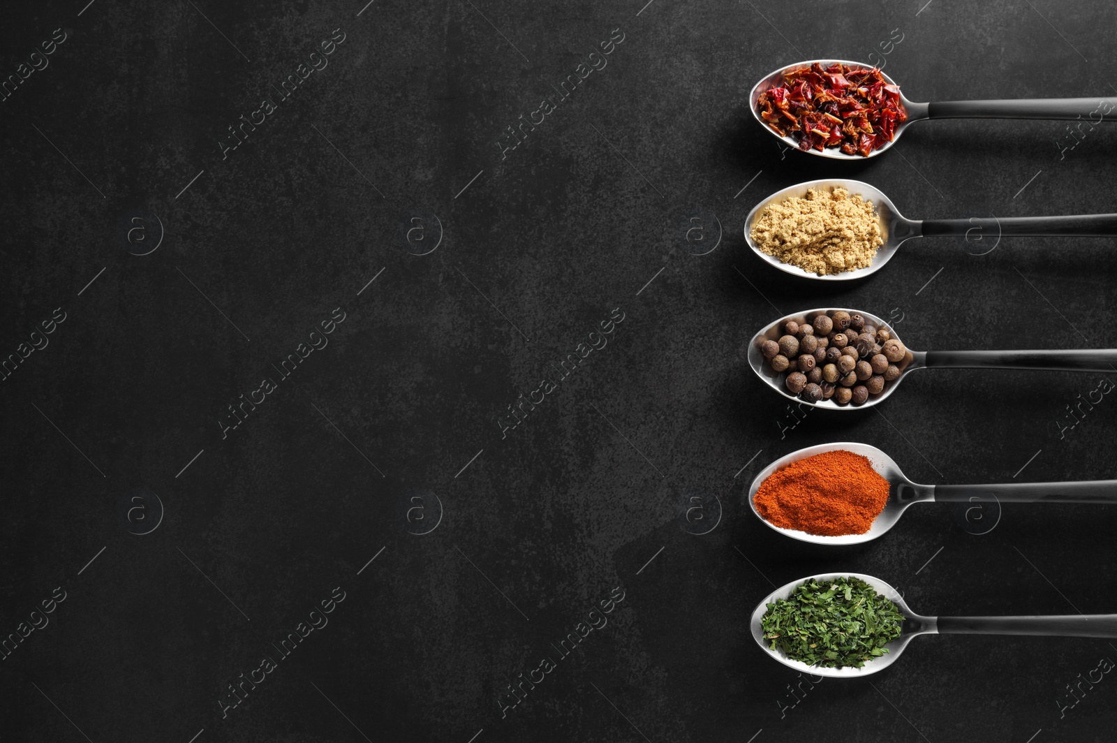 Photo of Metal spoons with different spices on black table, flat lay. Space for text
