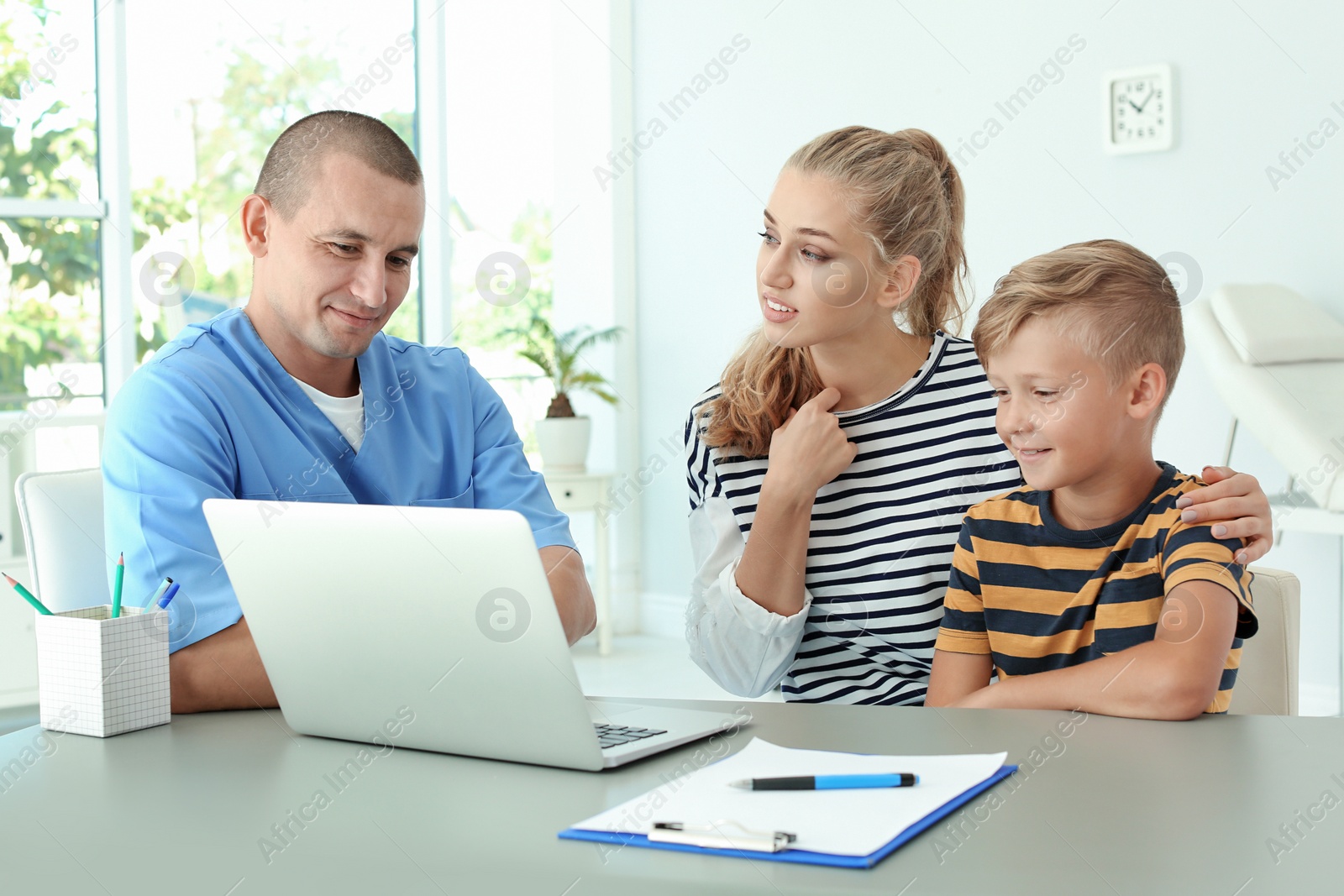 Photo of Male medical assistant explaining physical examination result to mother and child in clinic