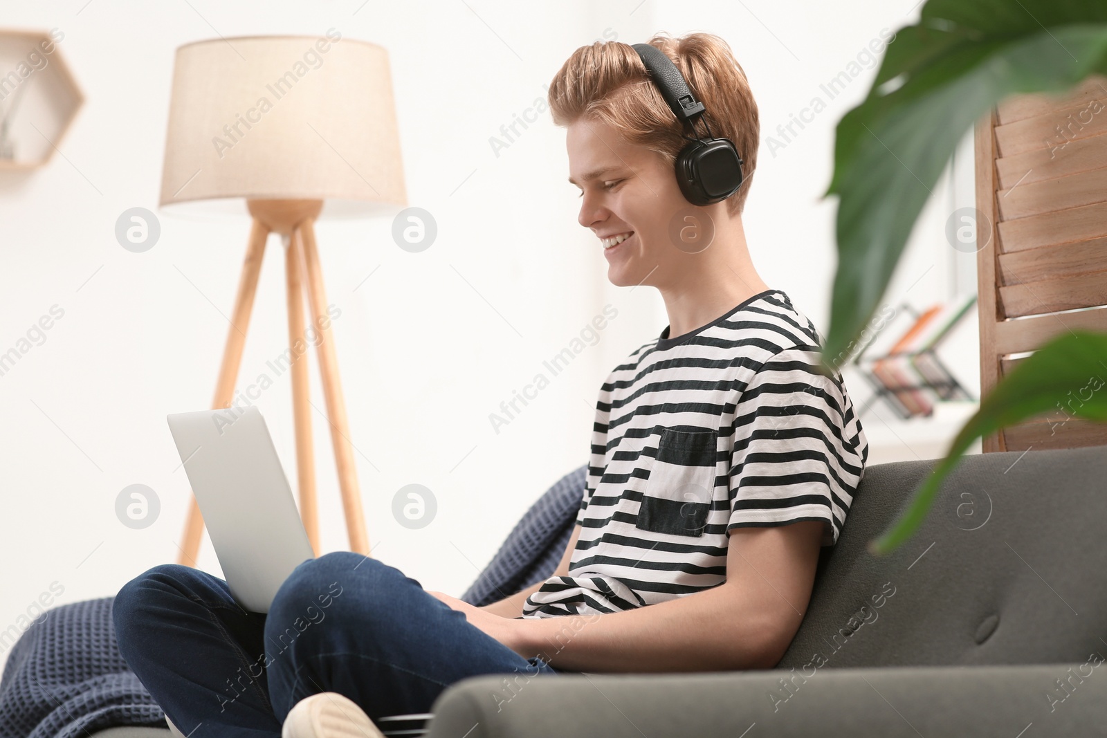 Photo of Online learning. Smiling teenage boy in headphones typing on laptop at home