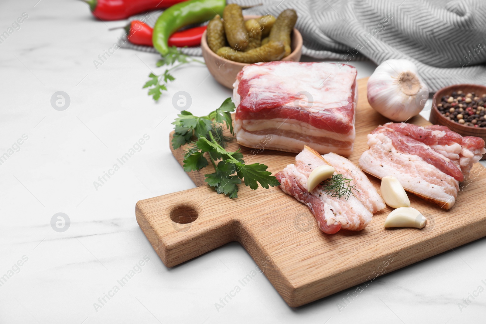 Photo of Board with pork fatback, spices and herbs on white marble table, space for text