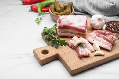 Photo of Board with pork fatback, spices and herbs on white marble table, space for text