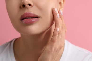 Woman with dry skin checking her face on pink background, closeup