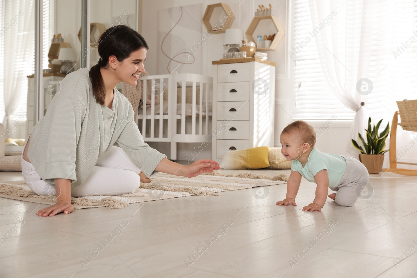 Photo of Happy young mother watching her cute baby crawl on floor at home