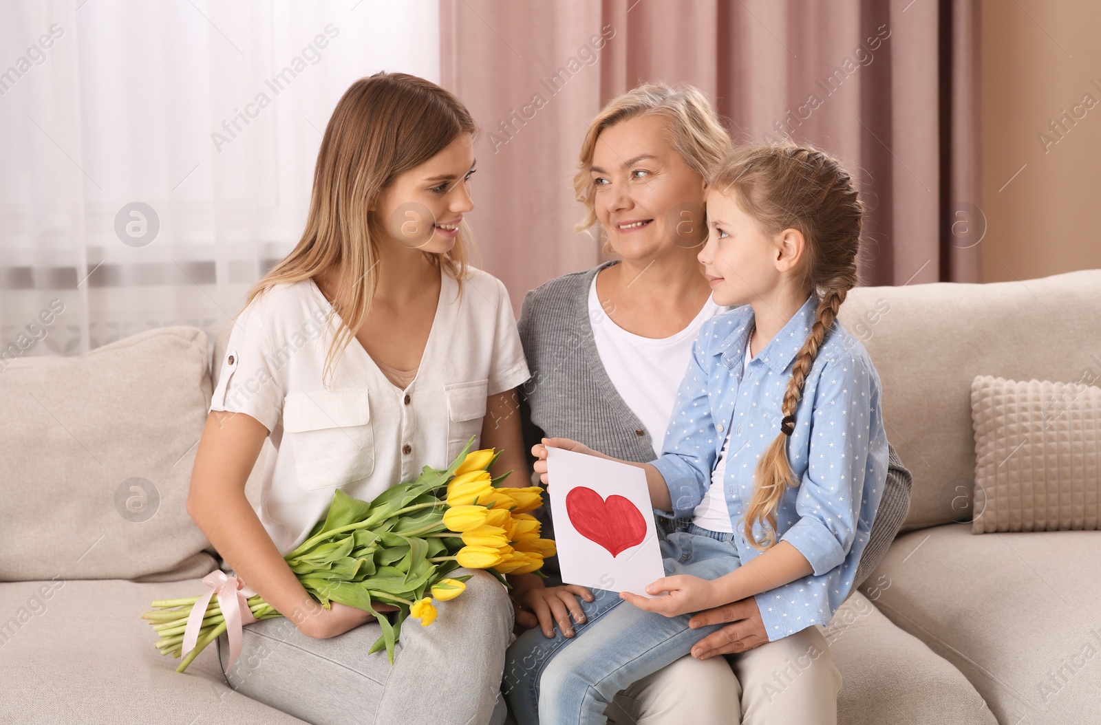 Photo of Little girl congratulating her mom and granny with flowers and postcard at home. Happy Mother's Day