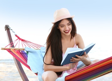 Photo of Young woman reading book in hammock at seaside