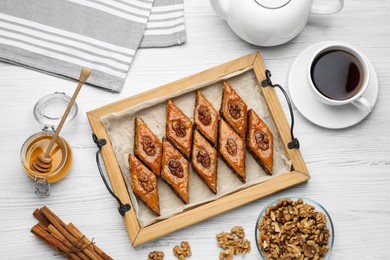 Photo of Delicious sweet baklava with walnuts, honey and hot tea on white wooden table, flat lay