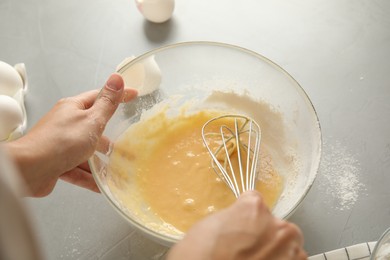 Woman whisking dough for cake at light grey table, closeup
