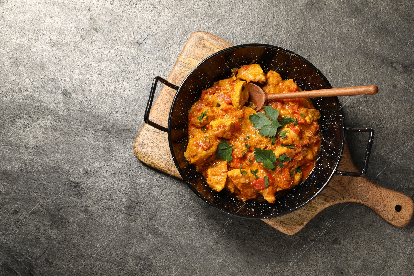 Photo of Delicious chicken curry in frying pan and spoon on grey table, top view. Space for text