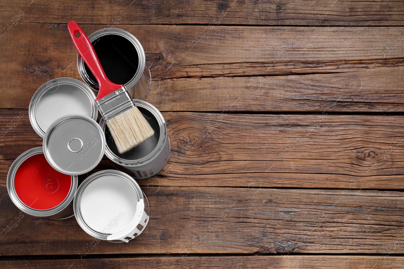 Photo of Cans of paints and brush on wooden table, flat lay. Space for text