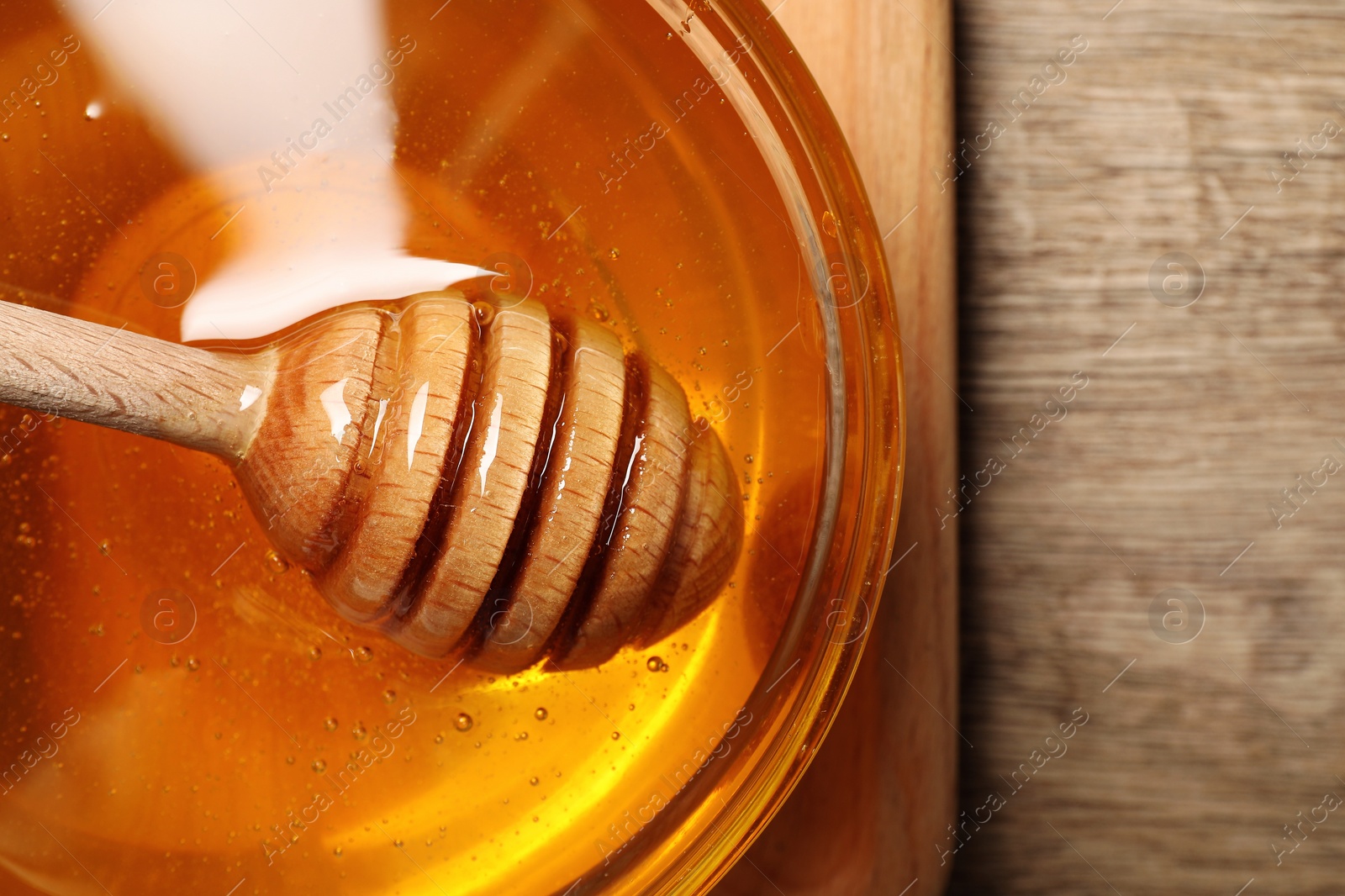 Photo of Honey with dipper in glass bowl on wooden table, top view. Space for text